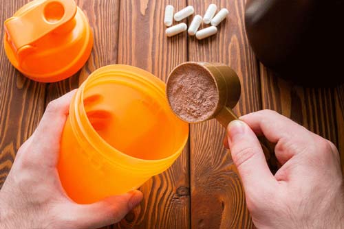 Supplements on table and protein powder being put into a shaker