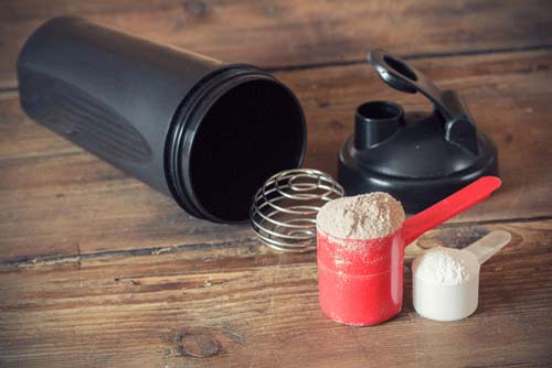 Closeup of two different kinds of protein powder and a shaker cup on its side