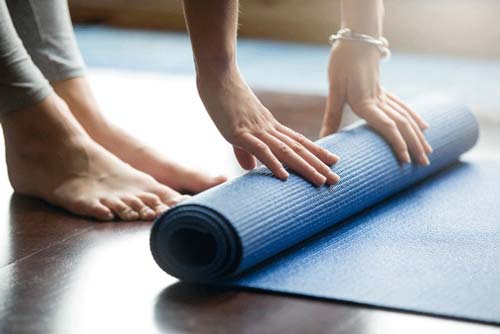 Close up of woman rolling out a blue yoga mat on the floor